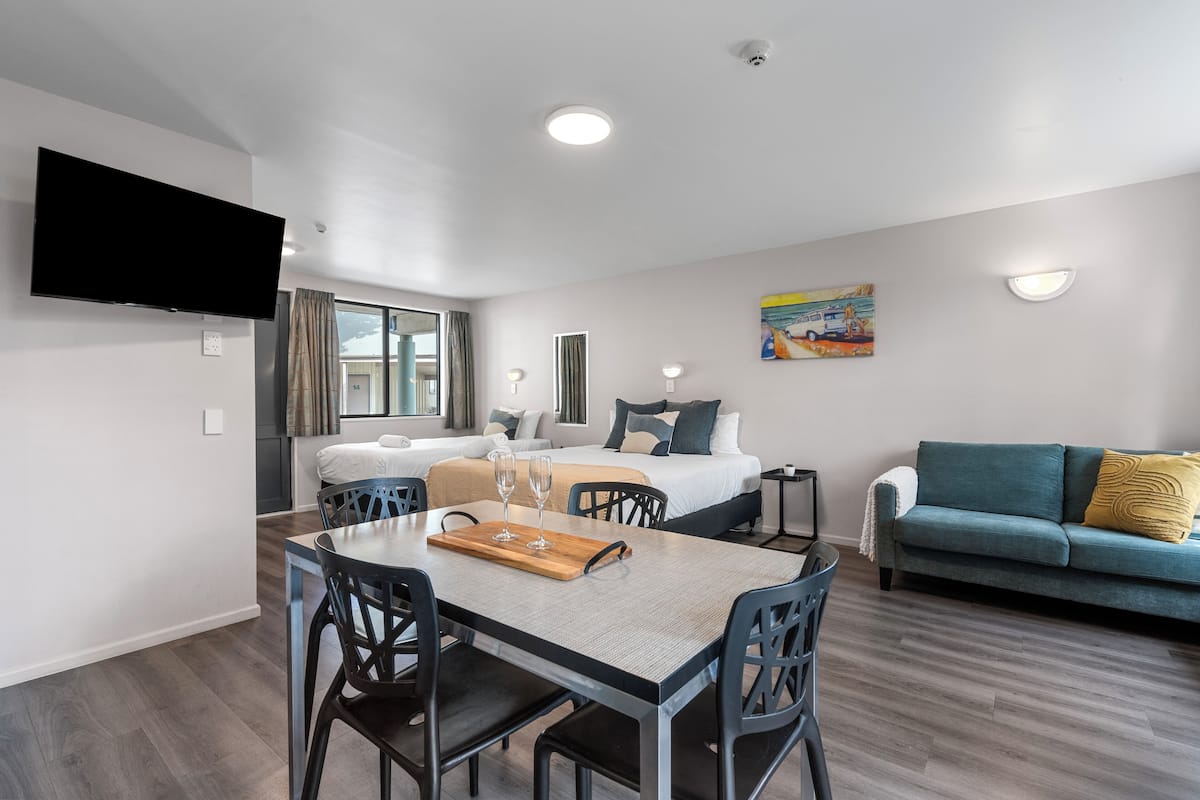 Una habitación de hotel moderna con una mesa de comedor, un sofá, una cama y un televisor montado en la pared.