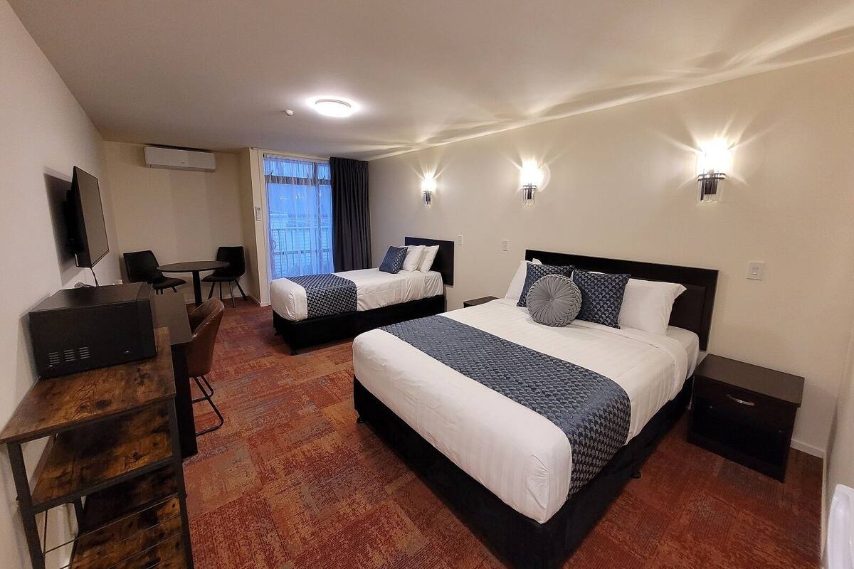 A hotel room with two beds, a desk, a chair, and a TV.