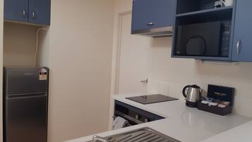 Cocina compacta con refrigerador integrado, microondas y cafetera sobre la encimera.
