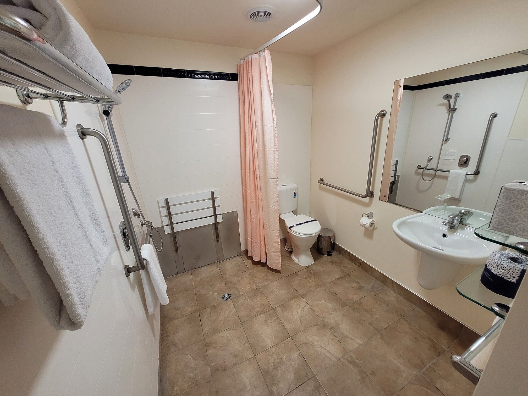 A bathroom with a shower, toilet, and sink. There are grab bars near the shower and a towel rack.