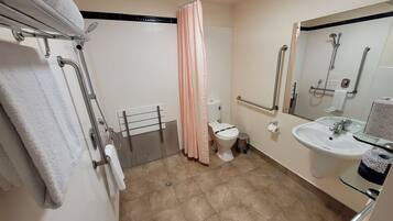 A bathroom with a shower, toilet, and sink. There are grab bars near the shower and a towel rack.