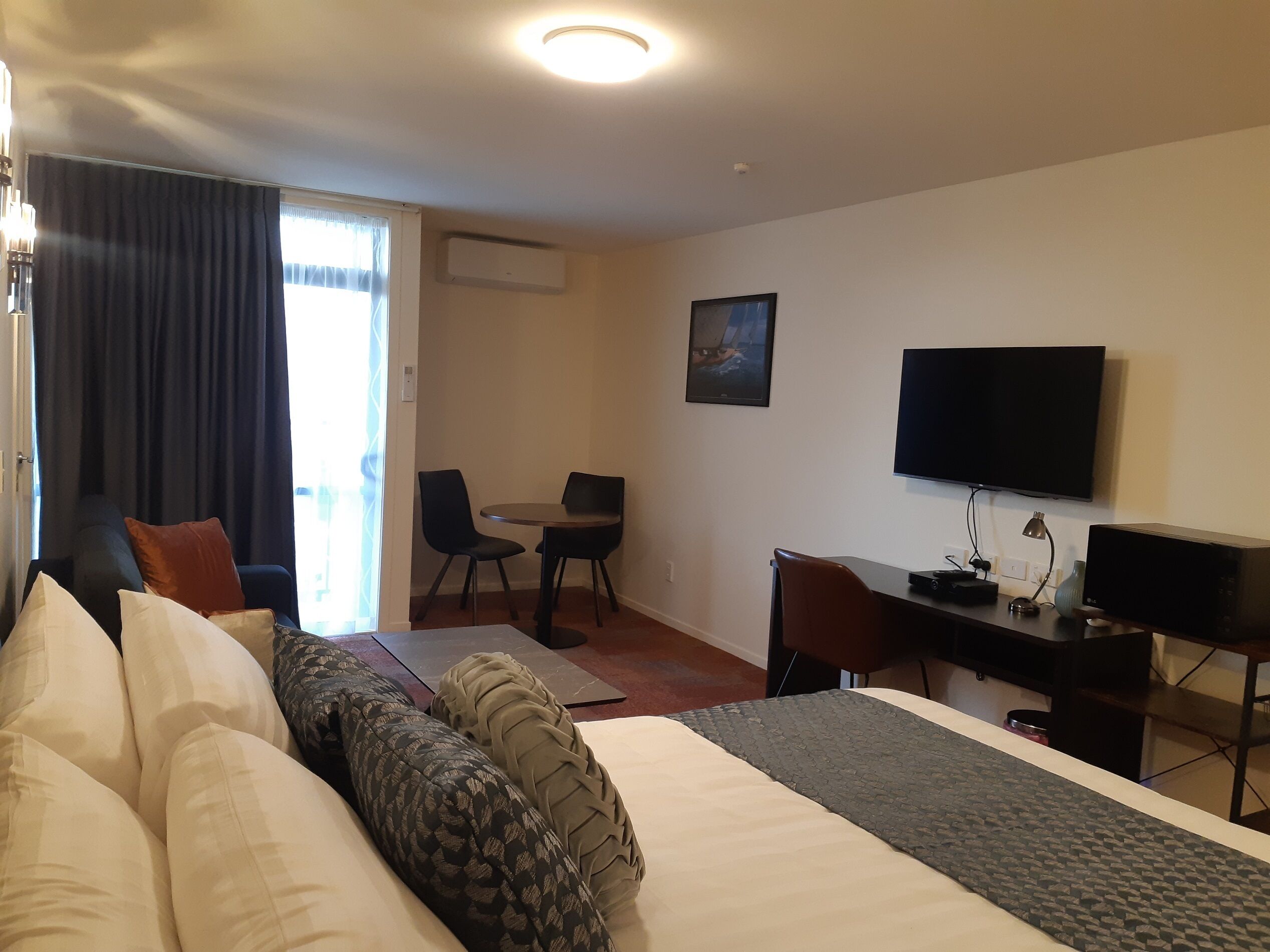 Ein Hotelzimmer mit Bett, Schreibtisch, Stuhl, Fernseher und einem Fenster mit Vorhängen.