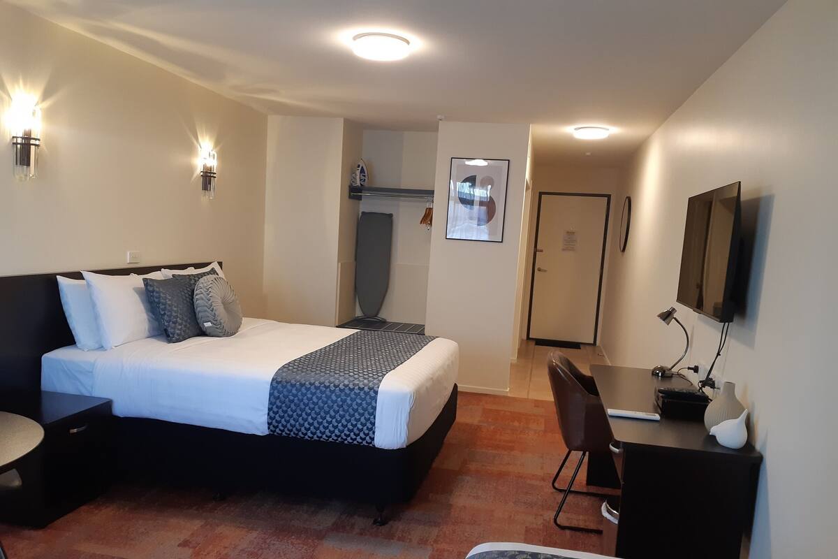 A hotel room with a bed, a desk, a chair, a flat-screen TV, and a door.