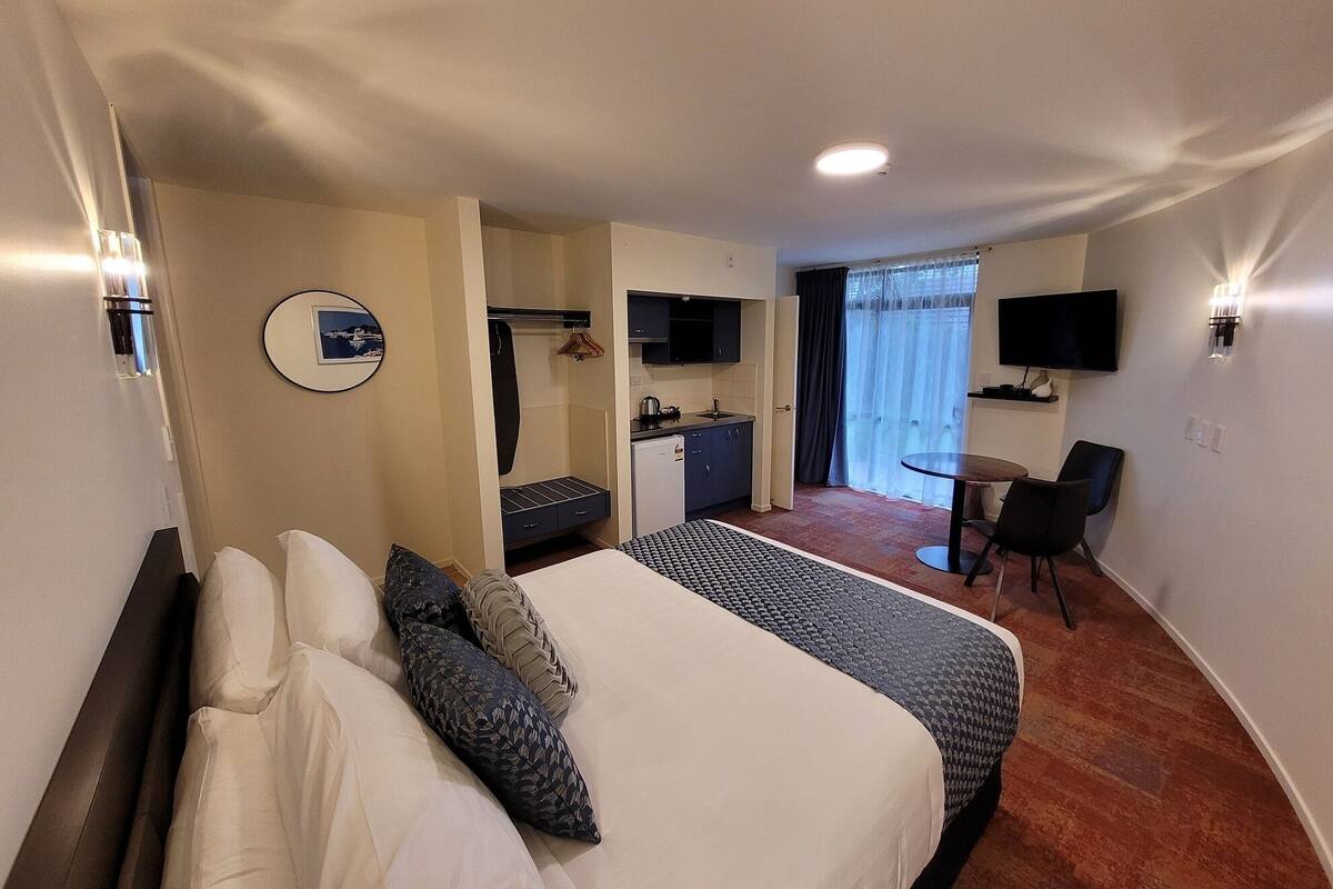 A hotel room with a bed, a desk, a chair, a TV, and a window with curtains.