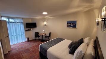 A hotel room with a bed, a desk with two chairs, a television, and a painting on the wall.