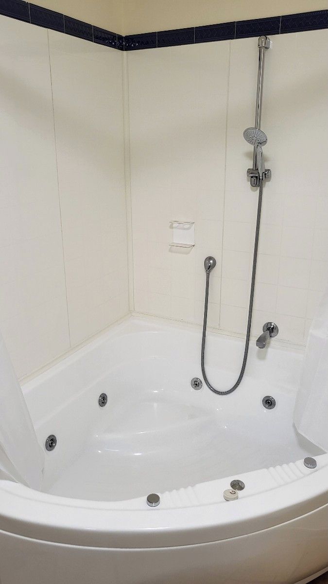 A white bathtub with a shower head and hose, set against a tiled wall with a black border.