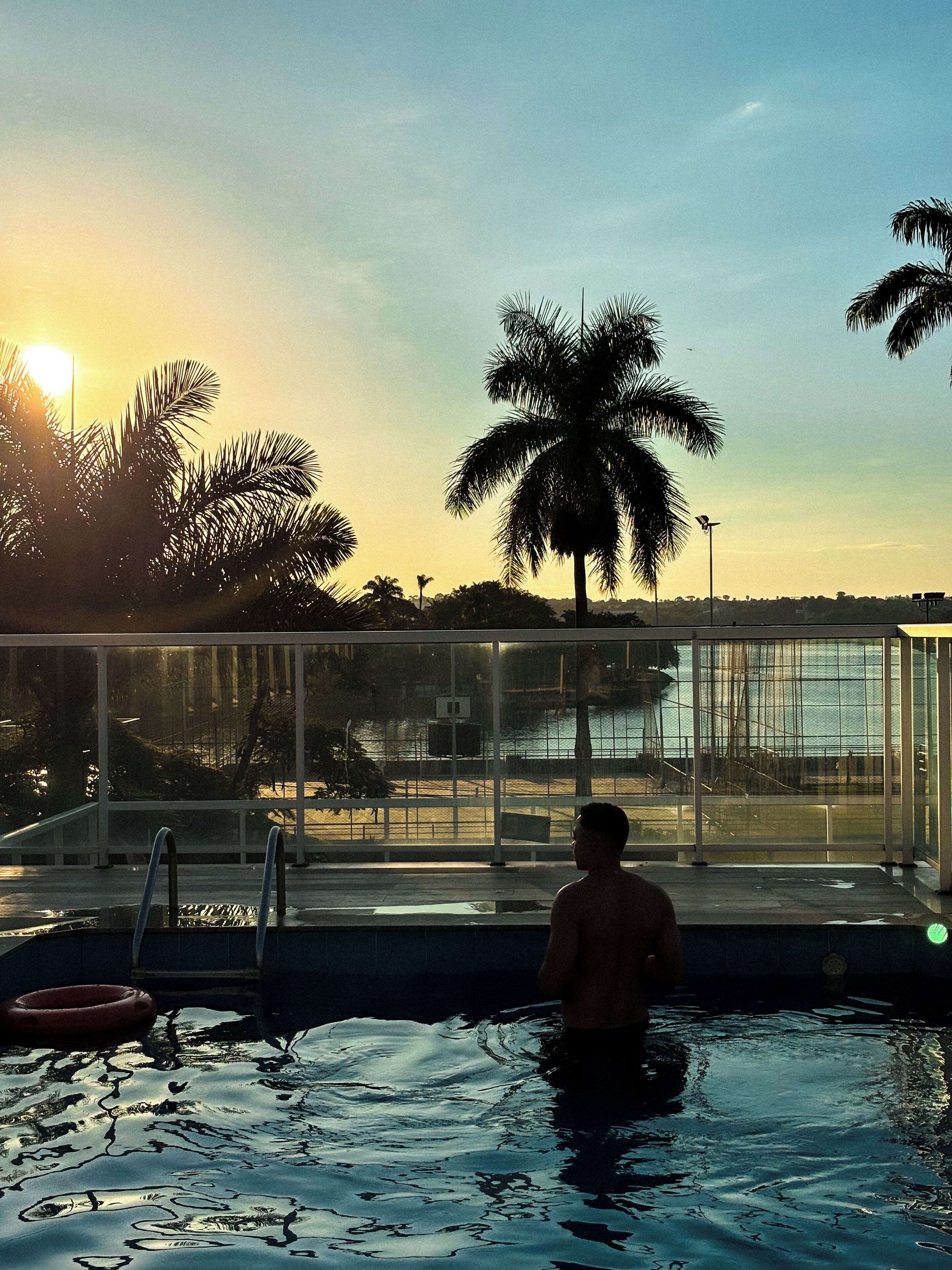 A man in a swimming pool with a view of palm trees and a sunset.