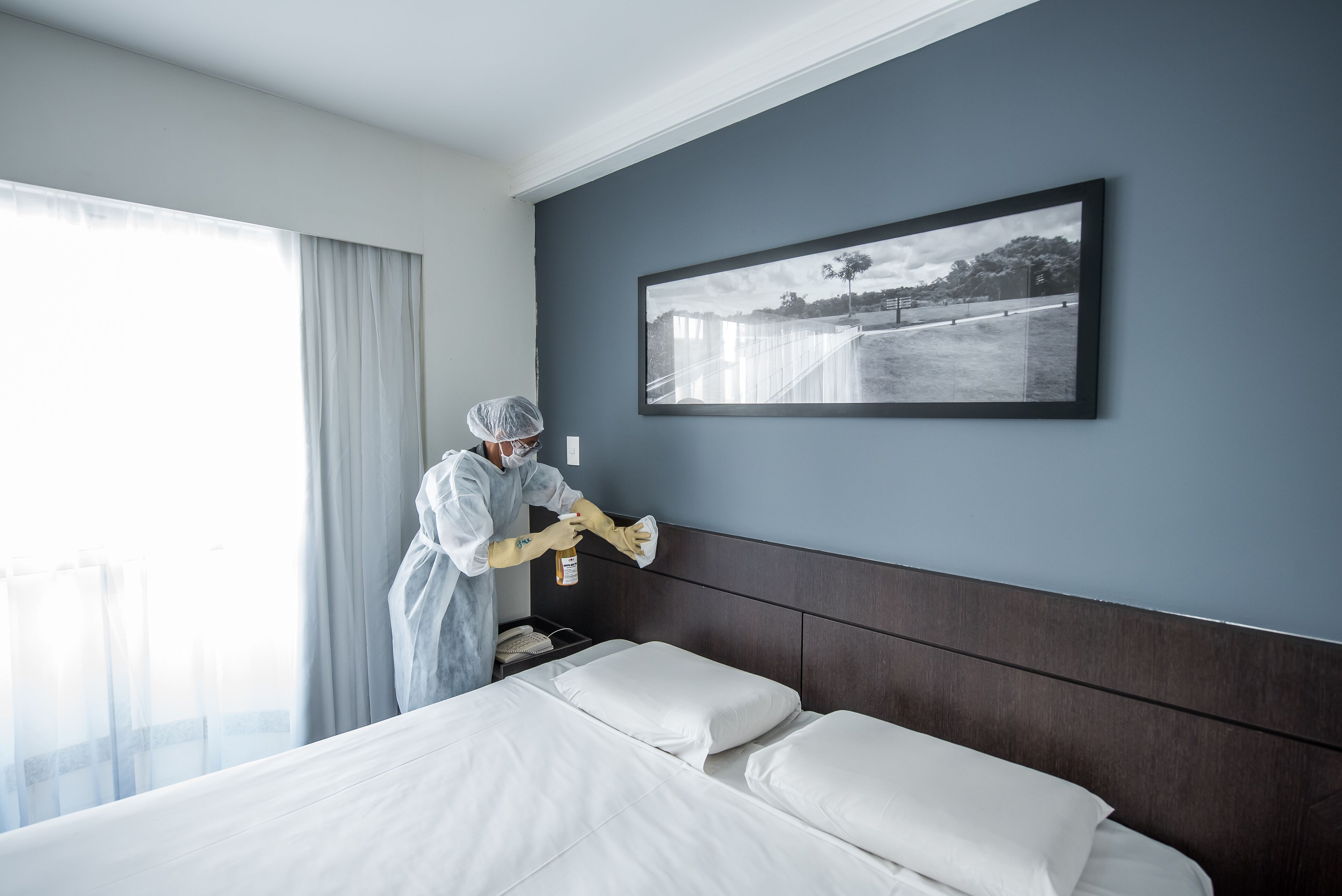 Habitación de hotel con una cama grande, cabecera, un cuadro enmarcado en la pared y una ventana con cortinas.