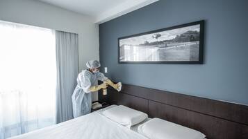Habitación de hotel con una cama grande, cabecera, un cuadro enmarcado en la pared y una ventana con cortinas.