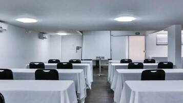 A conference room with rows of tables and chairs, white walls, and a door at the end.