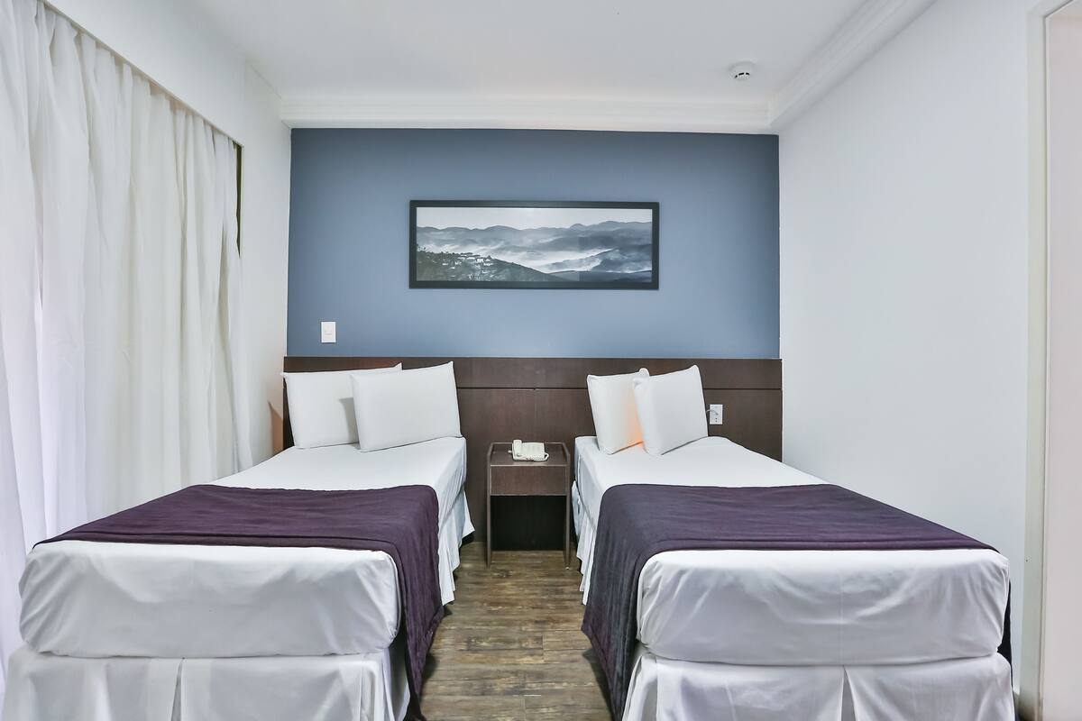Ein Hotelzimmer mit zwei Betten, einem Nachttisch, einem Telefon und einem gerahmten Bild an der Wand.