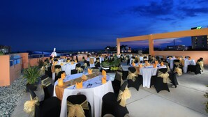 Een buitenterras met ronde tafels gedekt voor een formeel evenement, met zwarte stoelen met gouden linten en witte tafelkleden.