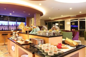 Disposição de buffet com diversos alimentos e acompanhamentos, área de bar com bebidas e área de estar com cadeiras e mesas.