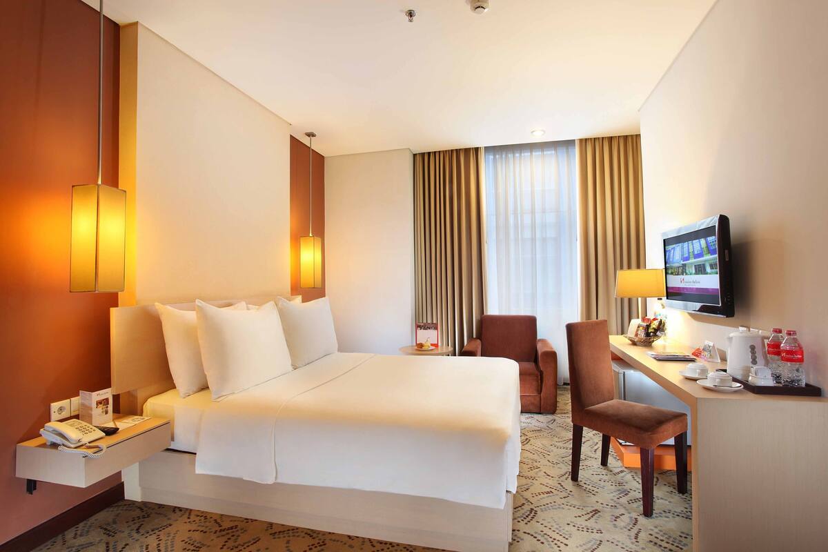 Een hotelkamer met een groot bed, een bureau met stoel, een televisietoestel en een minibar.