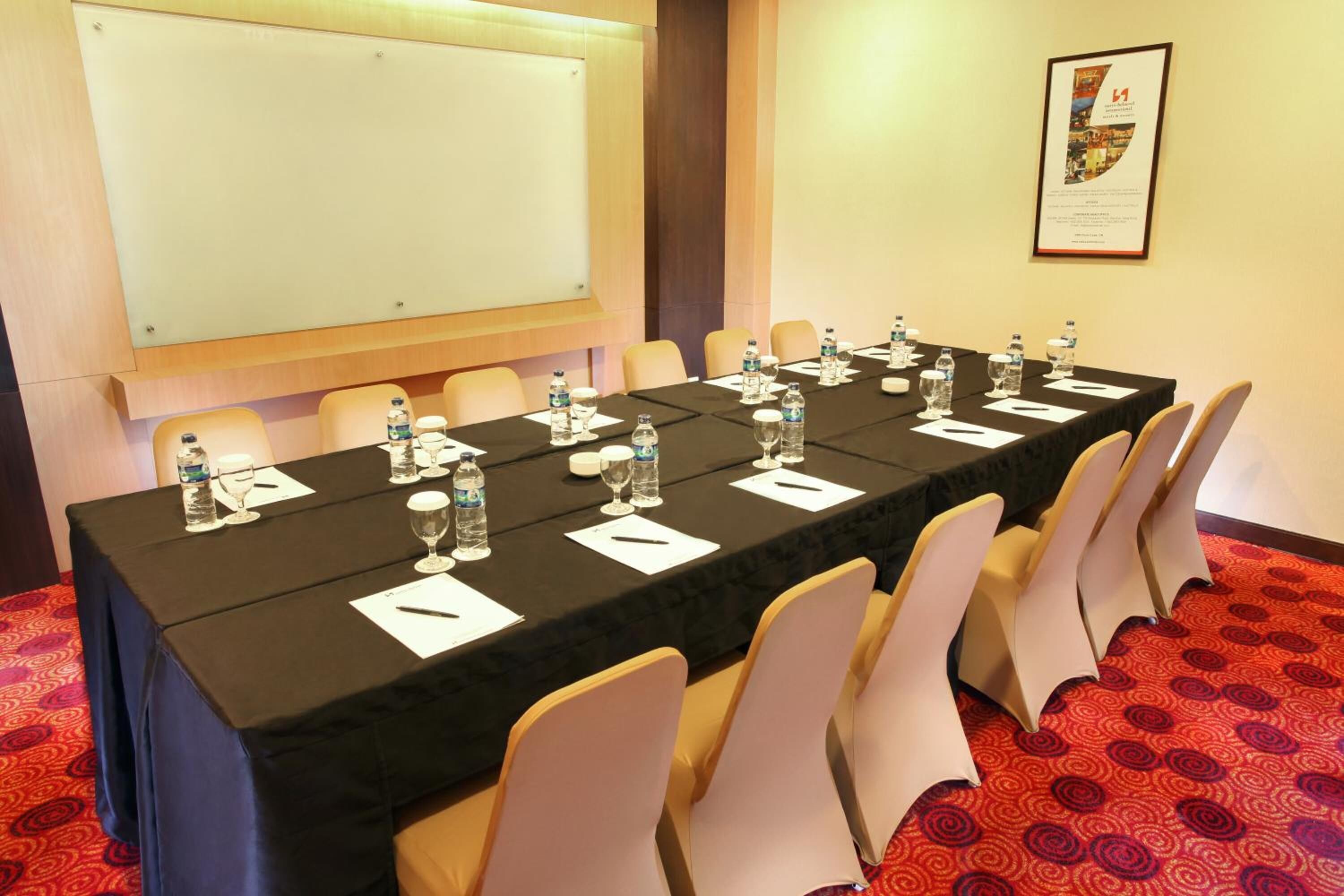 Un salón de conferencias con una larga mesa, sillas, botellas de agua, vasos y una pizarra.