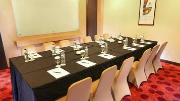 Un salón de conferencias con una larga mesa, sillas, botellas de agua, vasos y una pizarra.