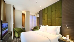 Een hotelkamer met een groot bed, een televisie, een groene fauteuil, een klein tafeltje en een telefoon op het nachtkastje.