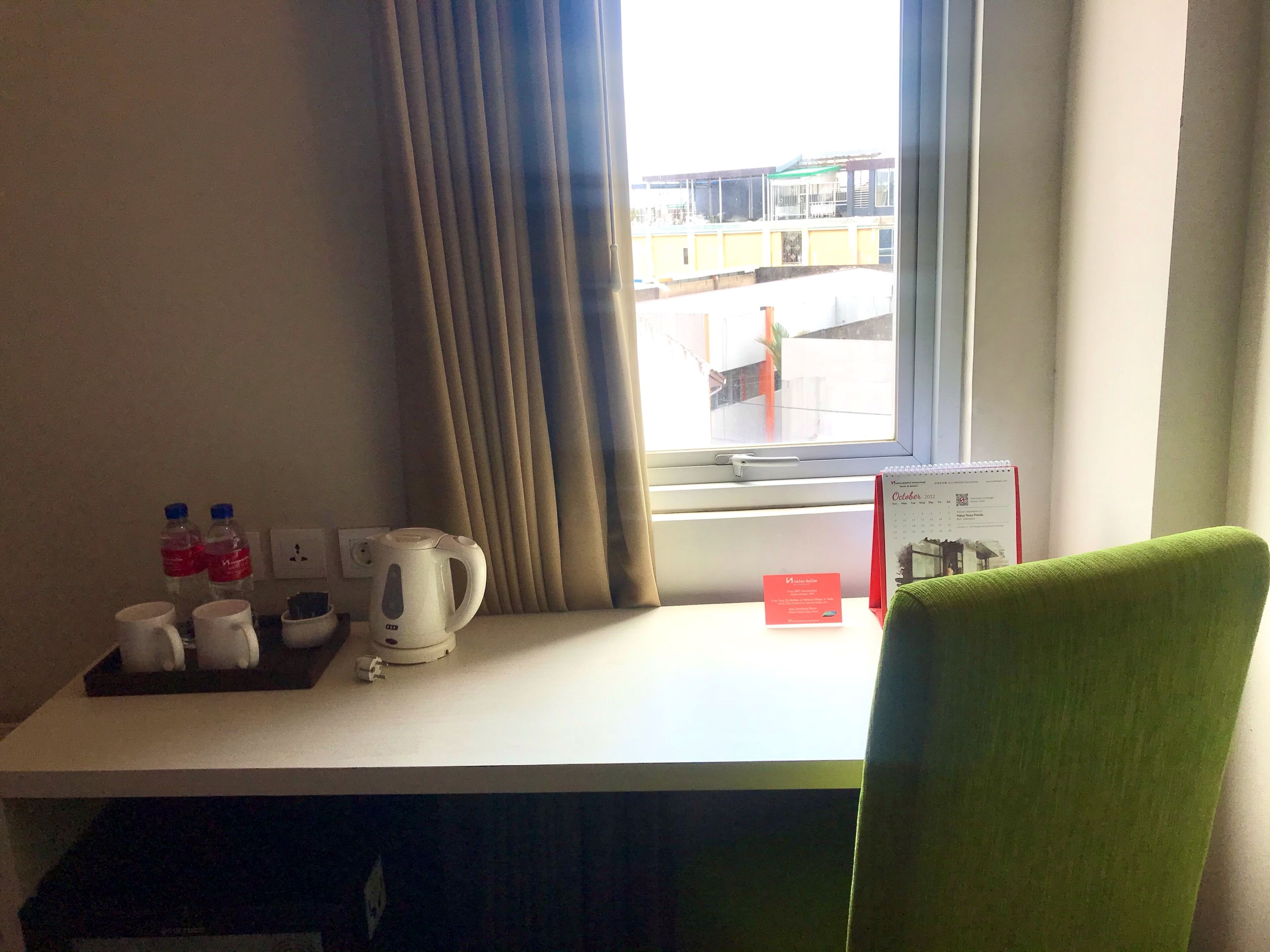 Une chambre d’hôtel équipée d’un bureau, d’une bouilloire, de deux bouteilles d’eau et d’un calendrier posé sur le rebord de la fenêtre.
