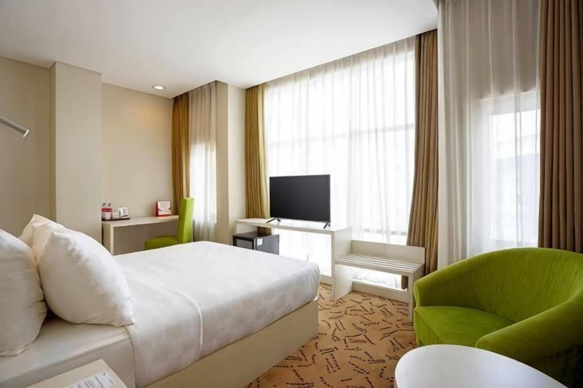 Een hotelkamer met een bed, een televisie, een bureau en een groene stoel.