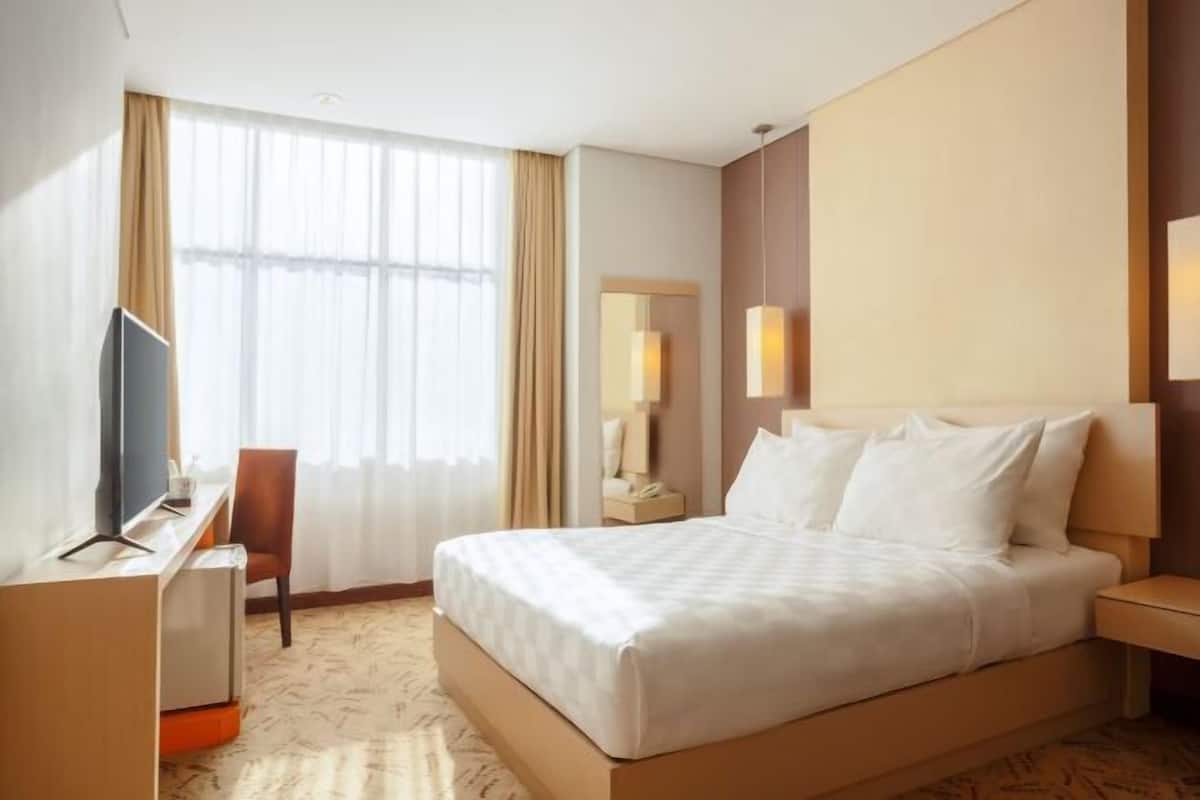 Een hotelkamer met een bed, een bureau, een stoel, een televisie en een raam met gordijnen.
