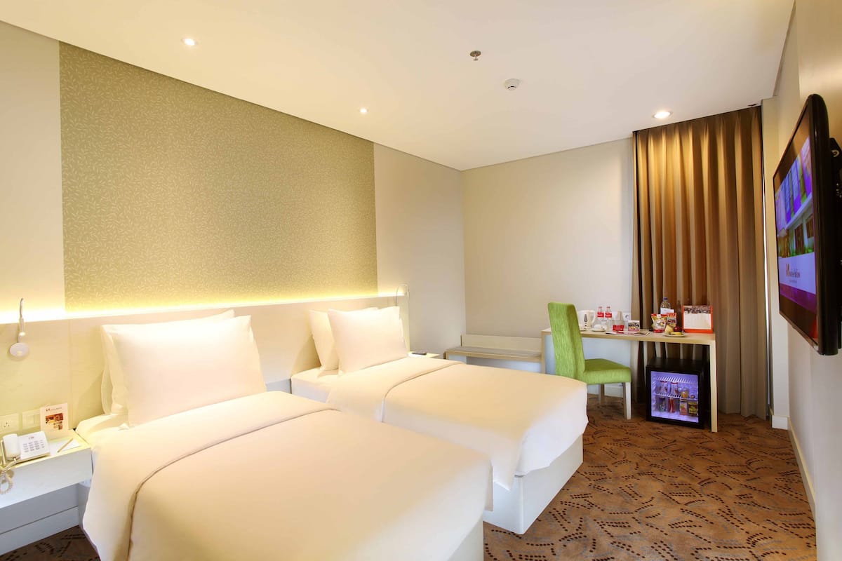 Een hotelkamer met twee bedden, een bureau met een computer, een televisietoestel en een minibar.