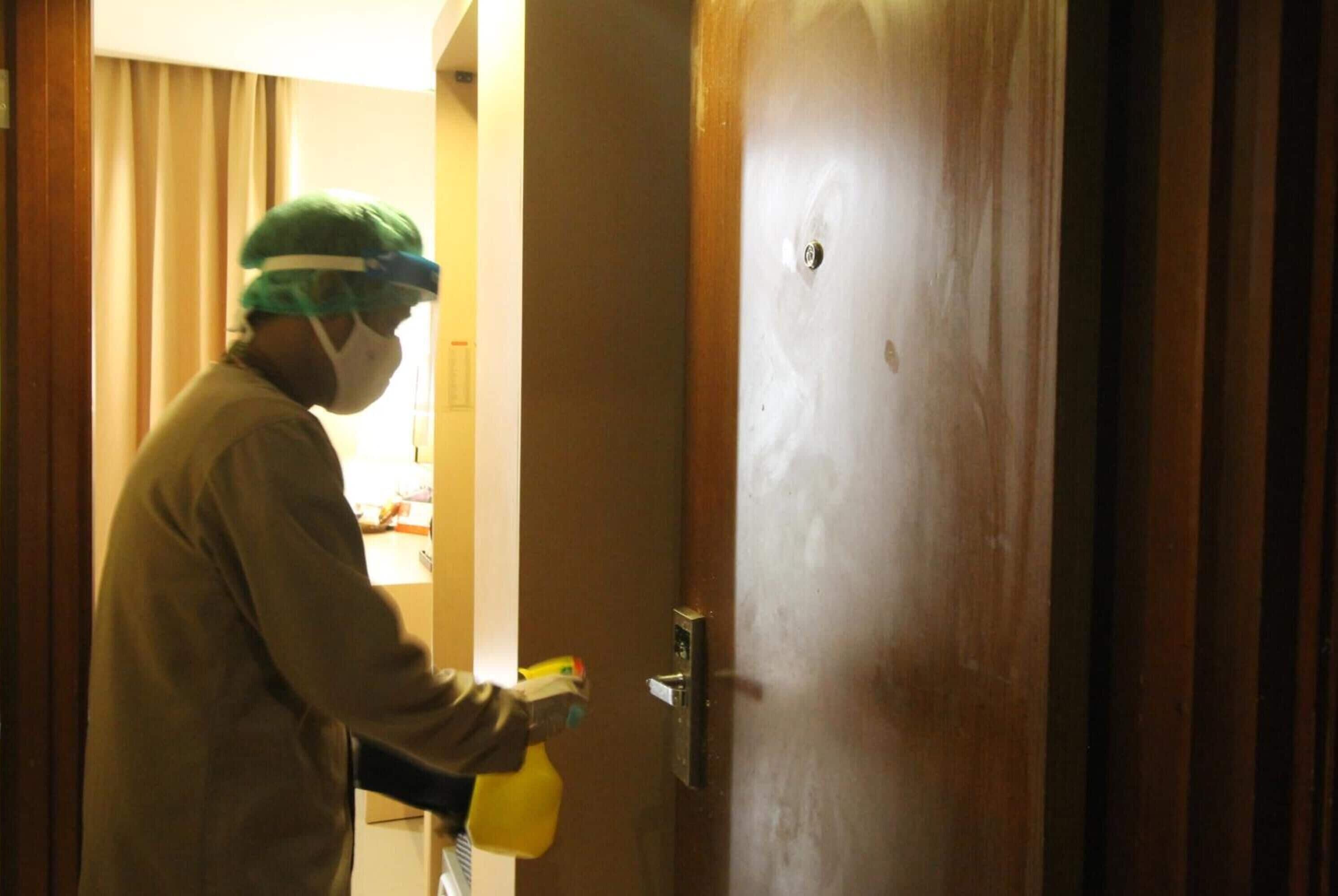 A person in a white coat and green cap spraying a yellow bottle on a door.