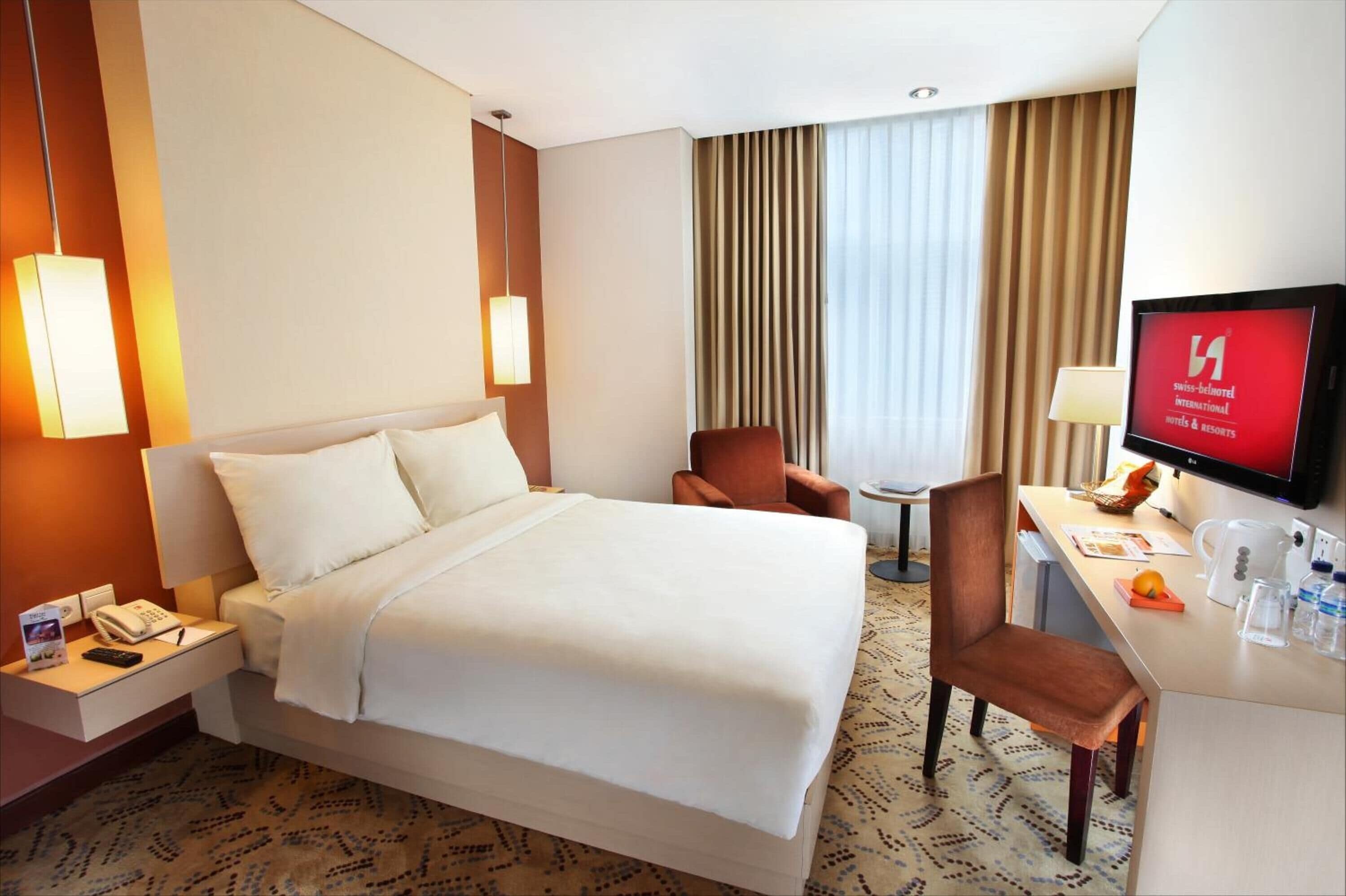 A hotel room with a bed, a desk with a television, a chair, and a small table.
