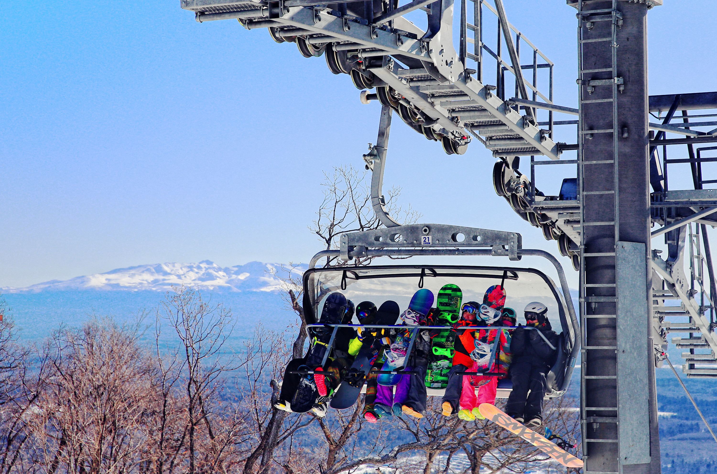 A ski lift with passengers and their snowboards, set against a mountainous backdrop.