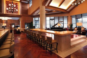 Un área de bar espaciosa con un piano, una barra de madera y varios taburetes.