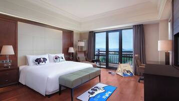 A hotel room with a large bed, a bench, a desk, and a balcony with a view.