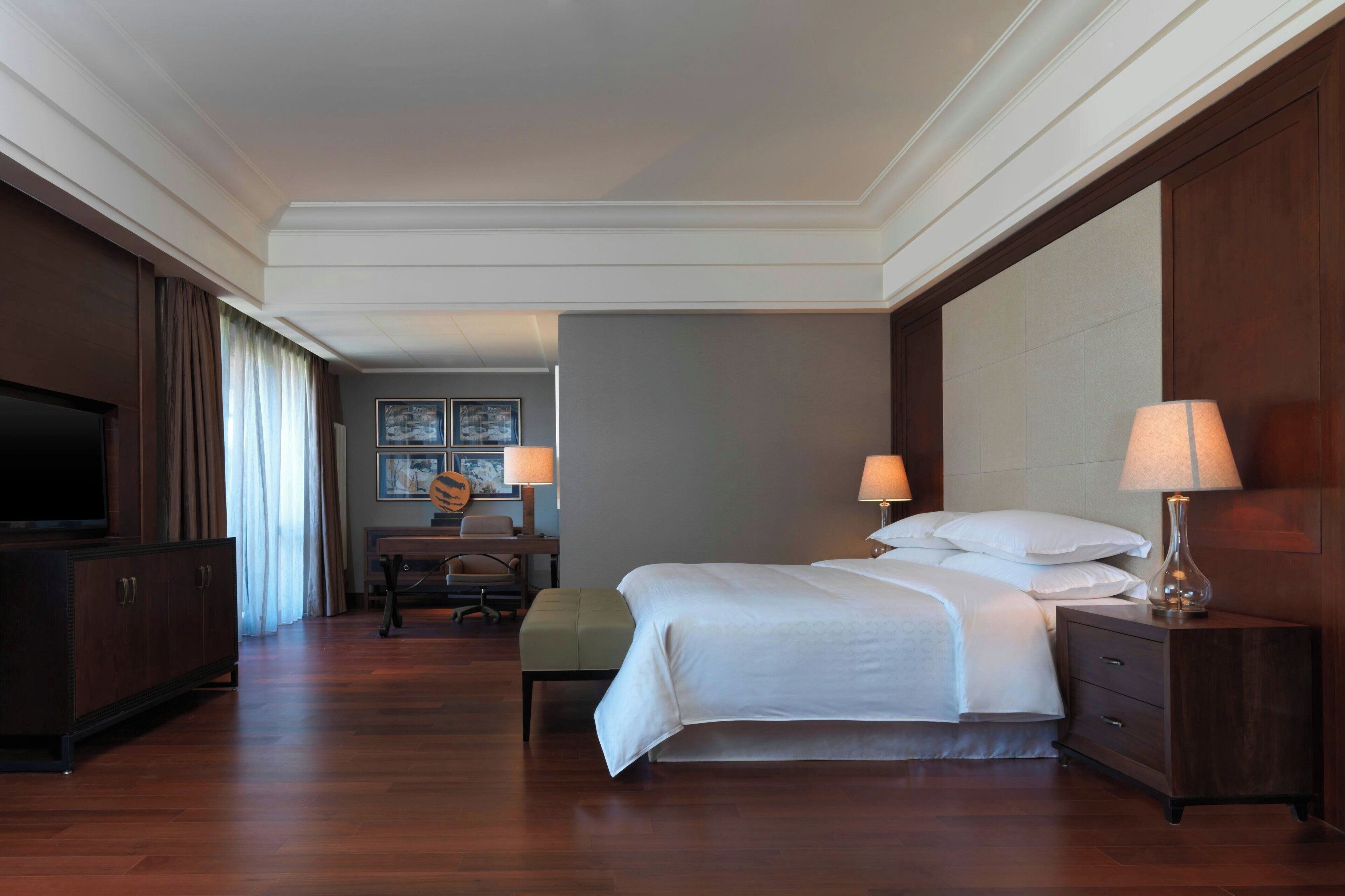 Une chambre d’hôtel avec un grand lit, des tables de chevet, une télévision, un bureau avec une chaise et une fenêtre avec des rideaux.
