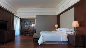 Une chambre d’hôtel avec un grand lit, des tables de chevet, une télévision, un bureau avec une chaise et une fenêtre avec des rideaux.