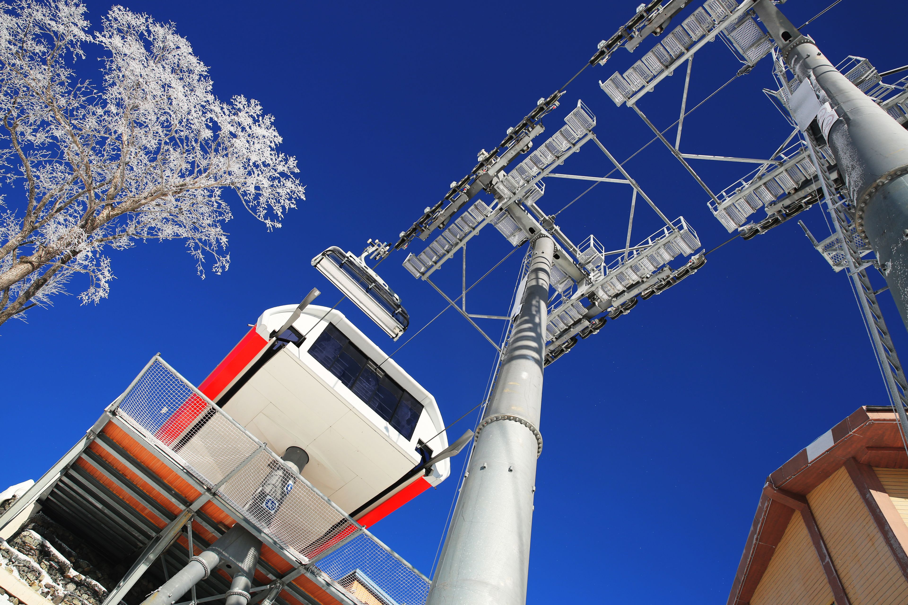 A high-angle view of a tall, industrial structure with a white and red vehicle on a platform, surrounded by metal frameworks and a clear blue sky.