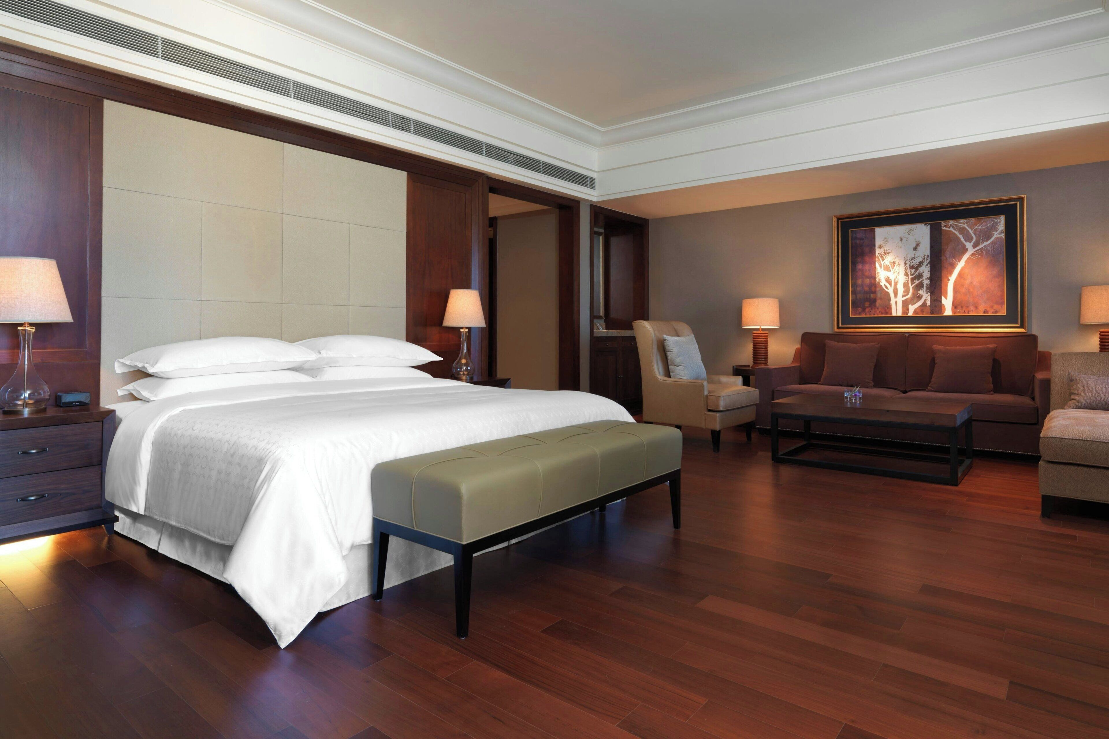 A hotel room with a large bed, a sofa, a coffee table, and a painting on the wall.