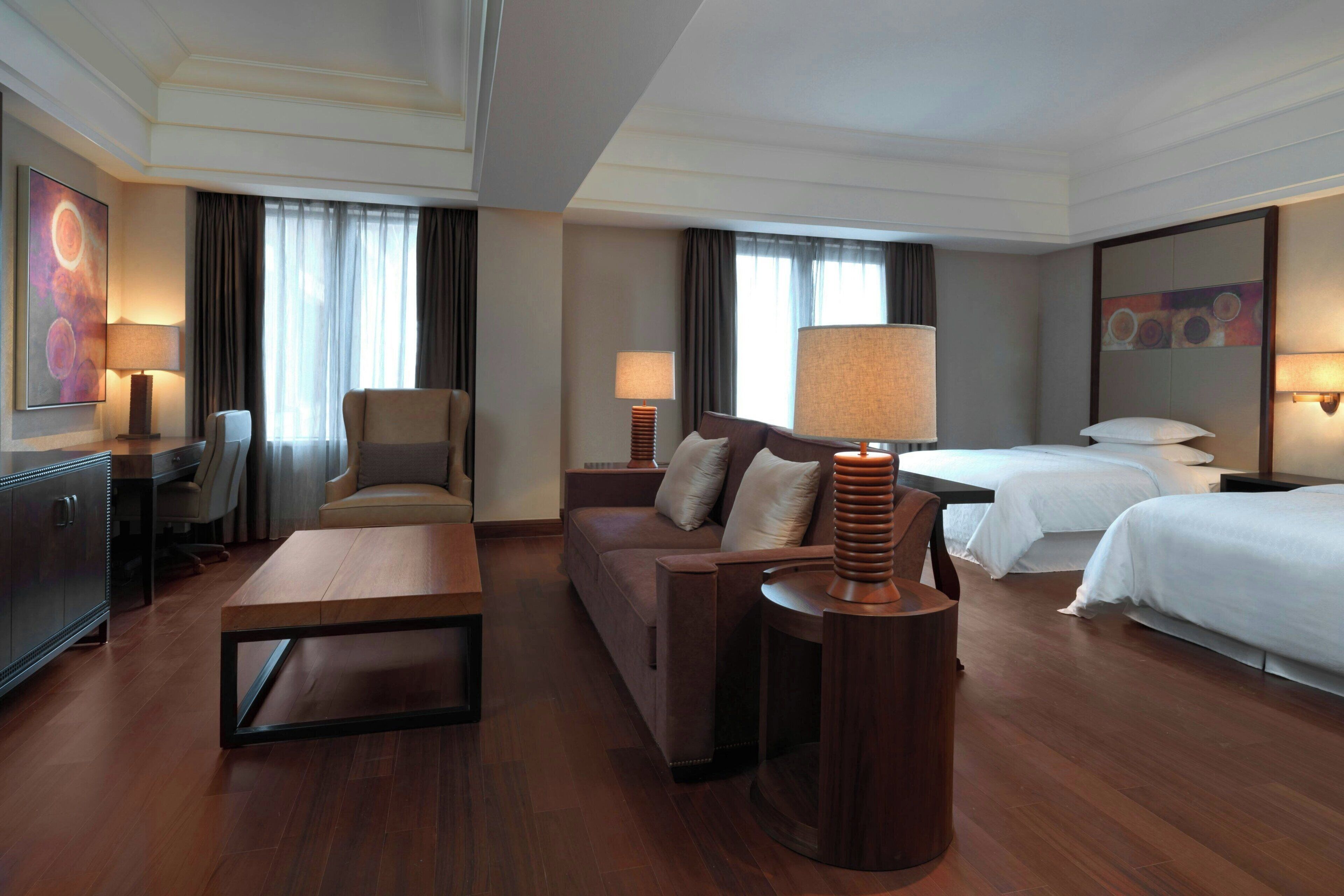 Una habitación de hotel con un sofá, dos camas, una mesita de madera y lámparas.