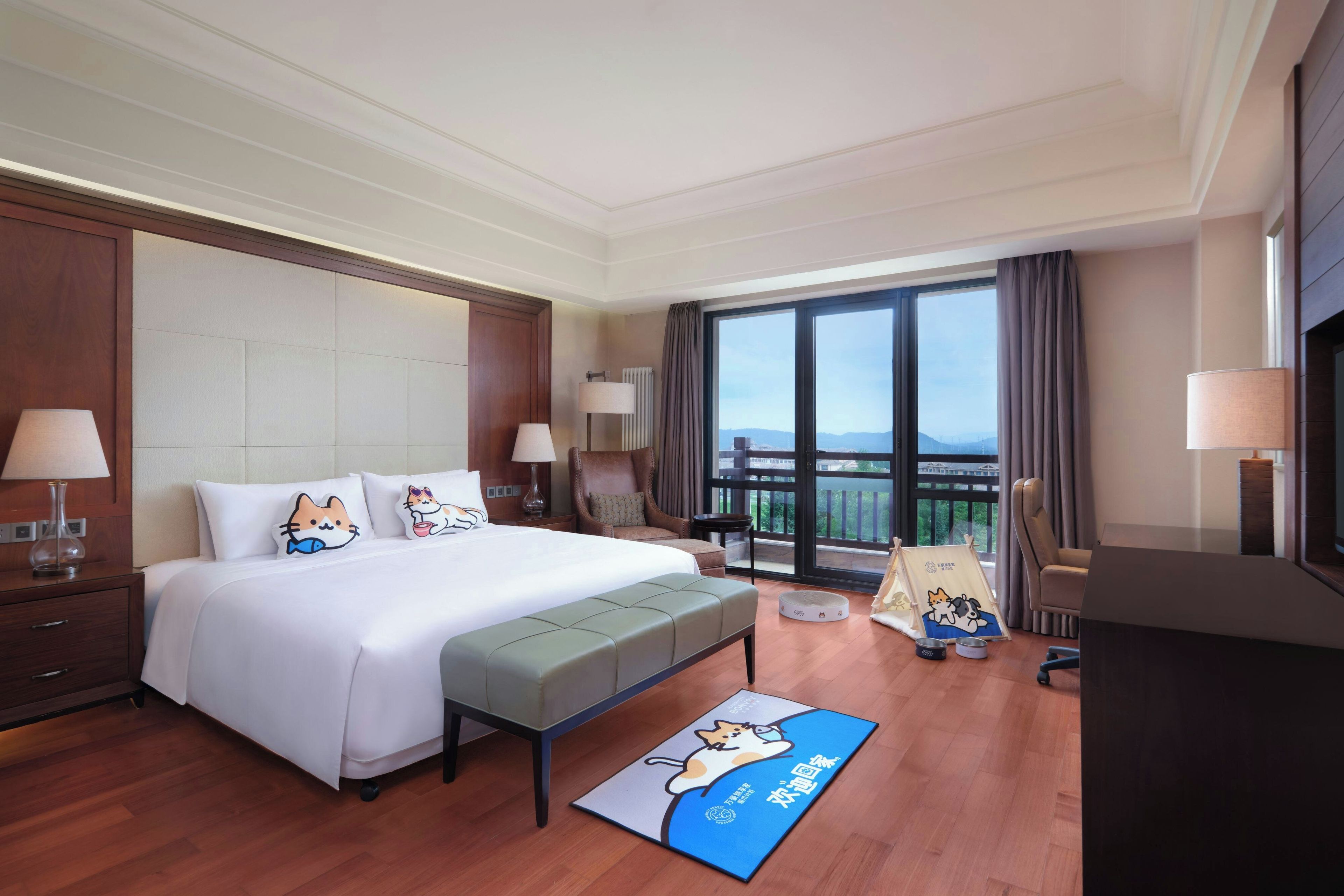 A hotel room with a large bed, a sitting area, a balcony with a view, and a pet bed.