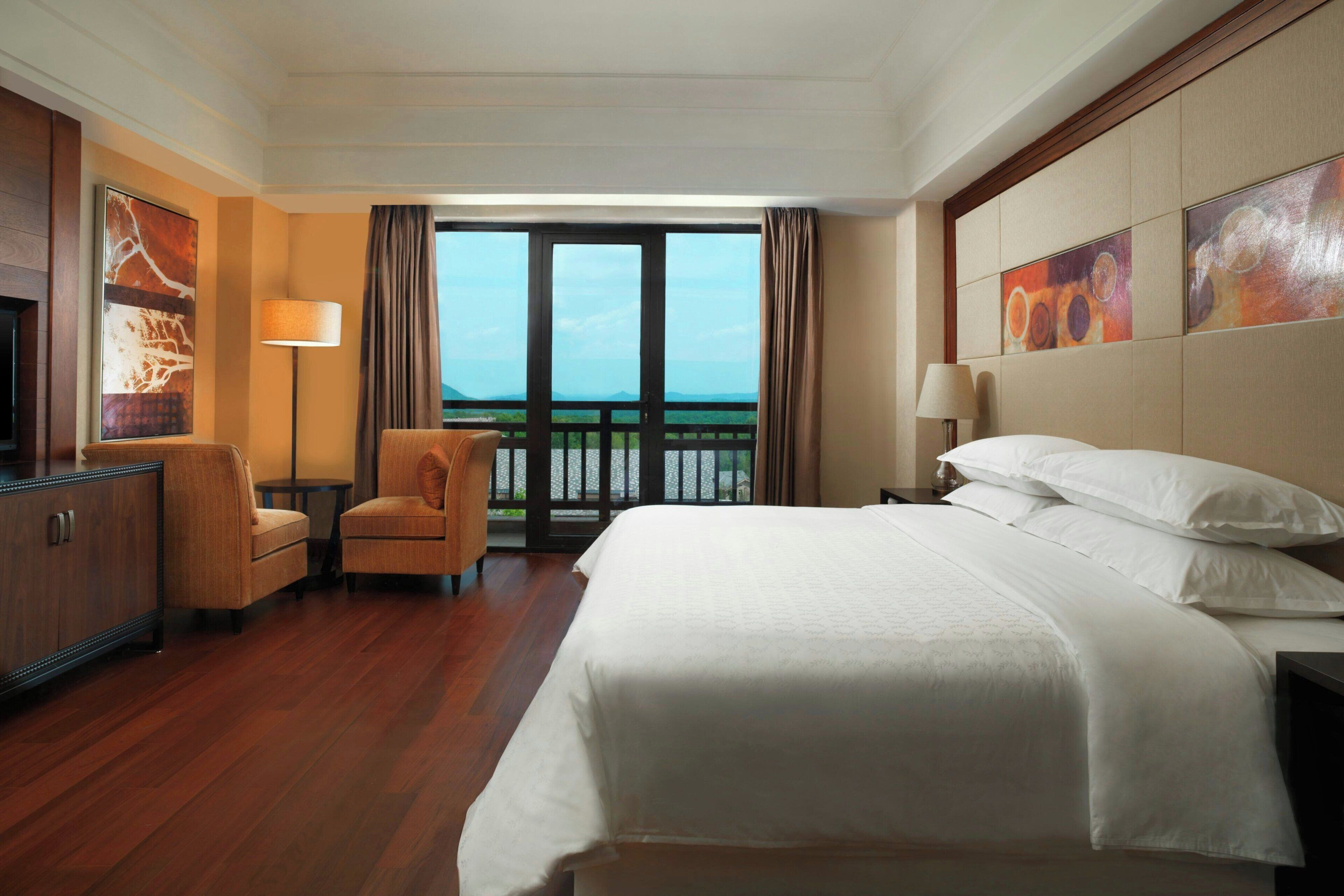 Une chambre d’hôtel avec un grand lit, un bureau, une chaise, une télévision et un balcon avec vue.
