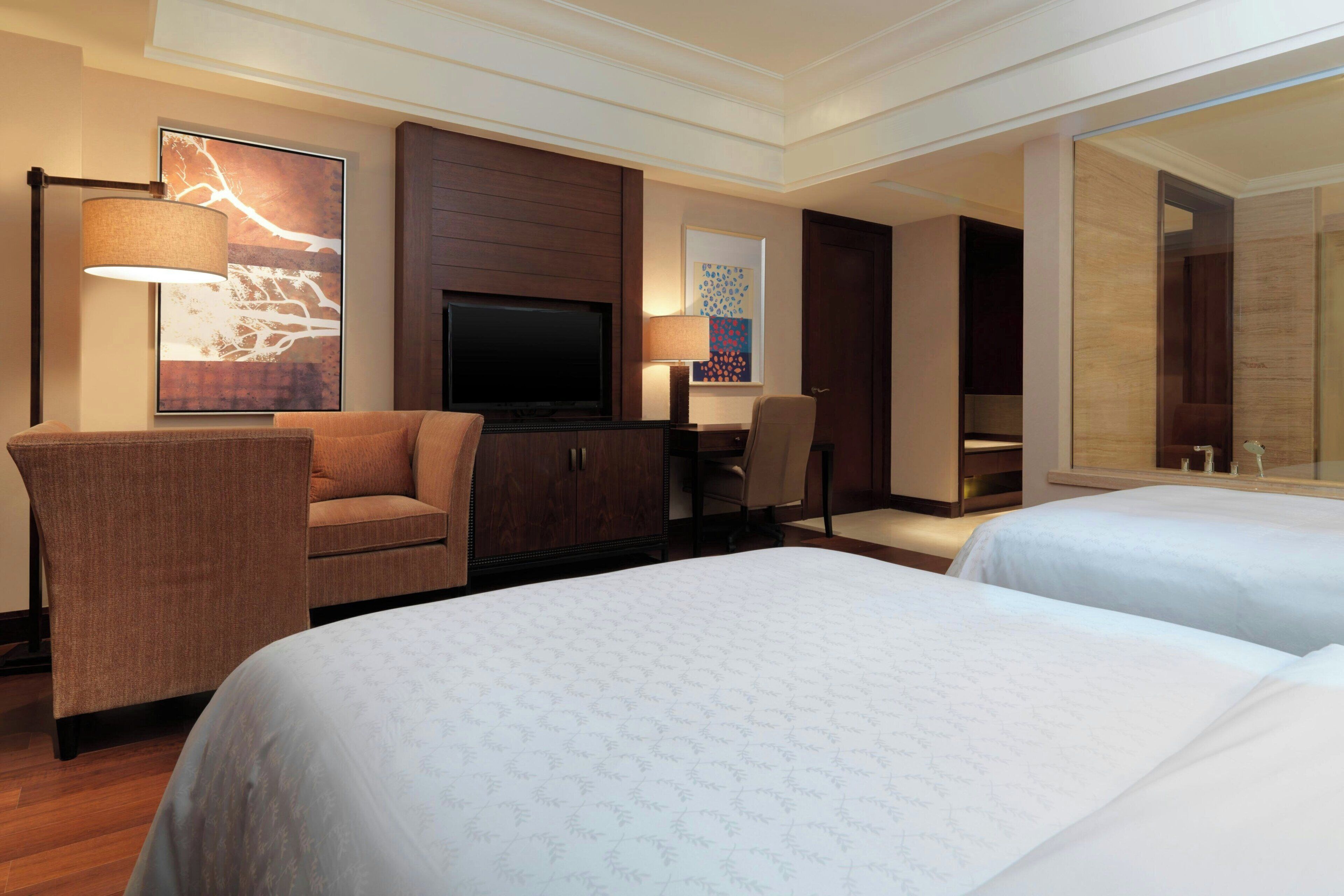 A hotel room with two beds, a TV, a desk, and a chair.