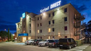 Hotel Kyriad Direct met een parkeerplaats en meerdere geparkeerde auto's ervoor.