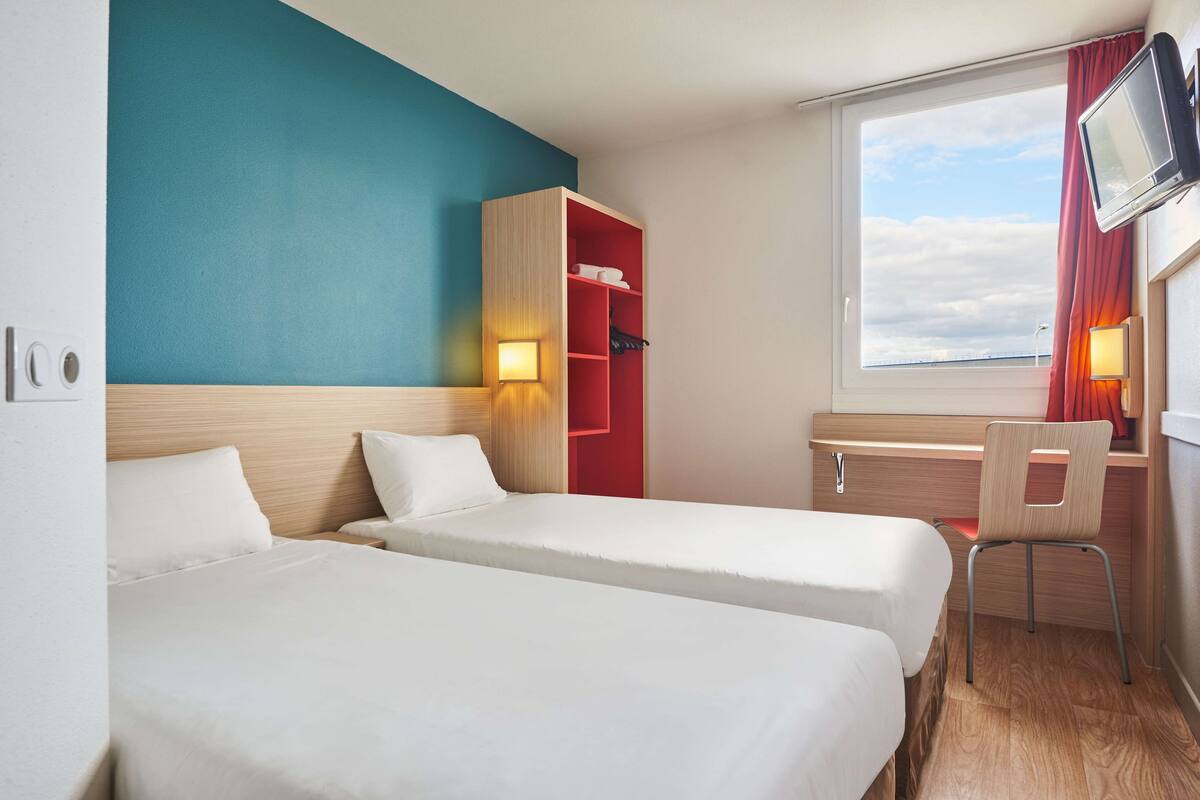 Een hotelkamer met twee bedden, een bureau, een stoel, een televisie en een raam met uitzicht.