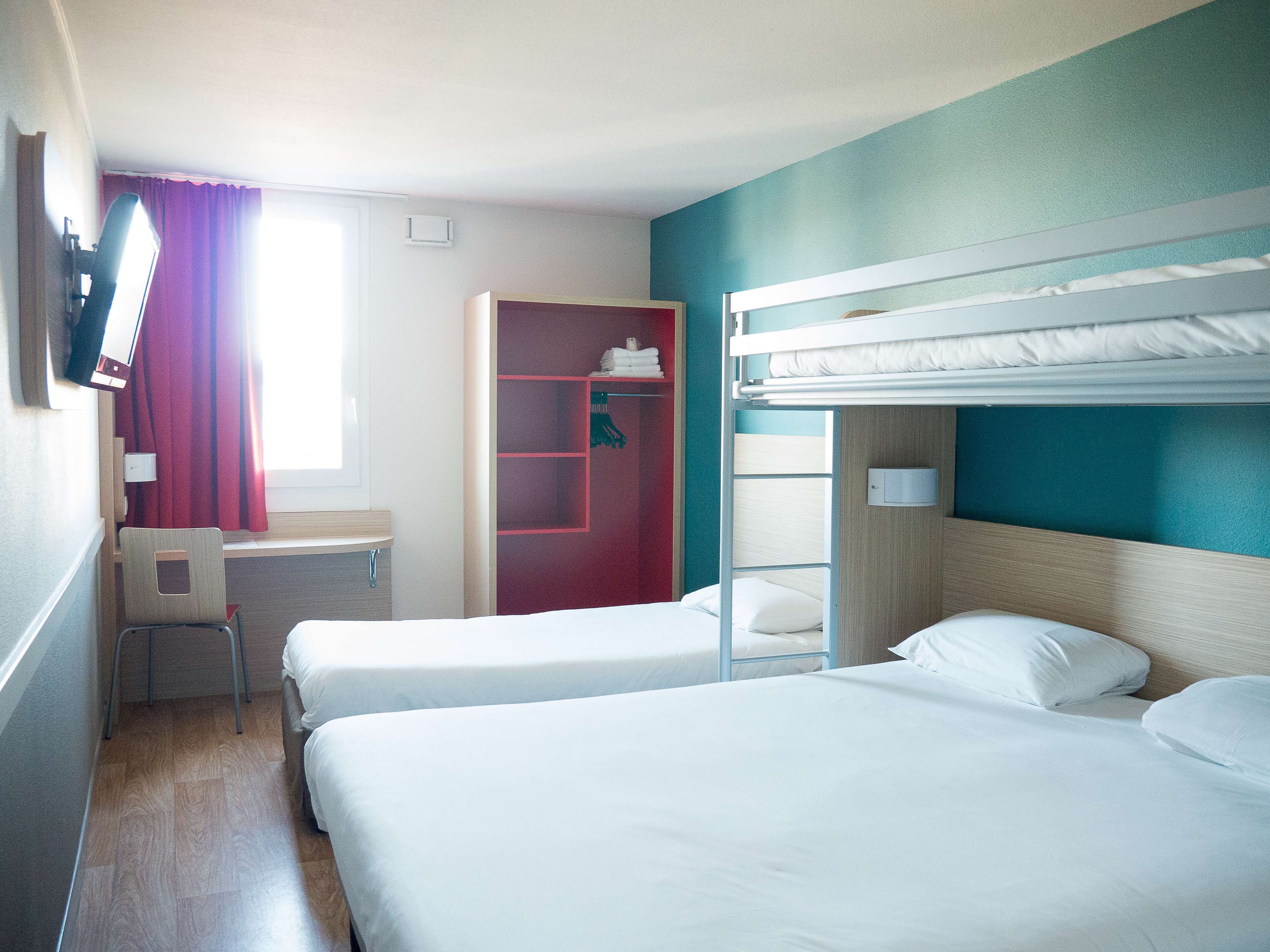 A hotel room with two beds, a desk, a chair, and a wardrobe.
