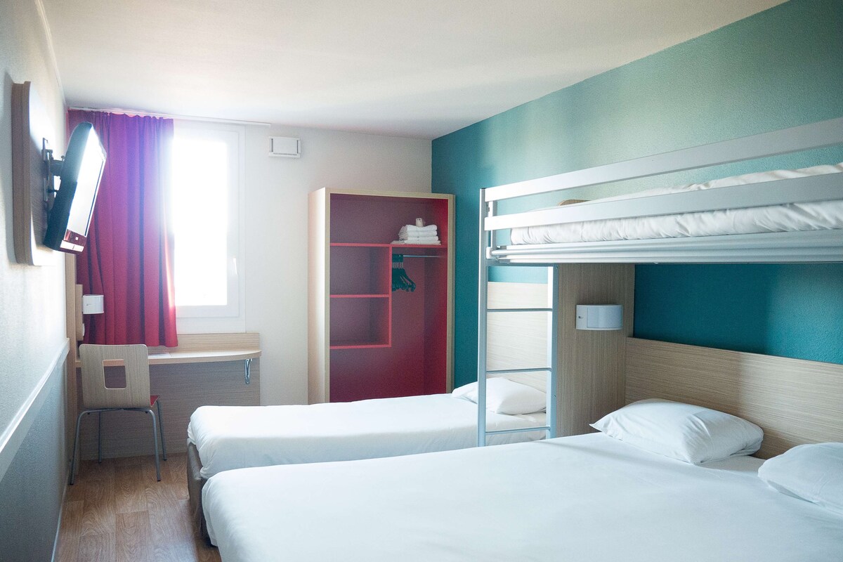 A hotel room with two beds, a desk, a chair, and a wardrobe.