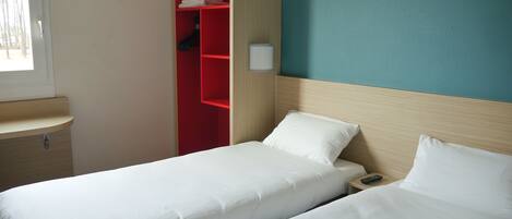 Habitación de hotel con dos camas individuales, un armario rojo, una mesita de noche pequeña y una ventana con vistas a árboles.
