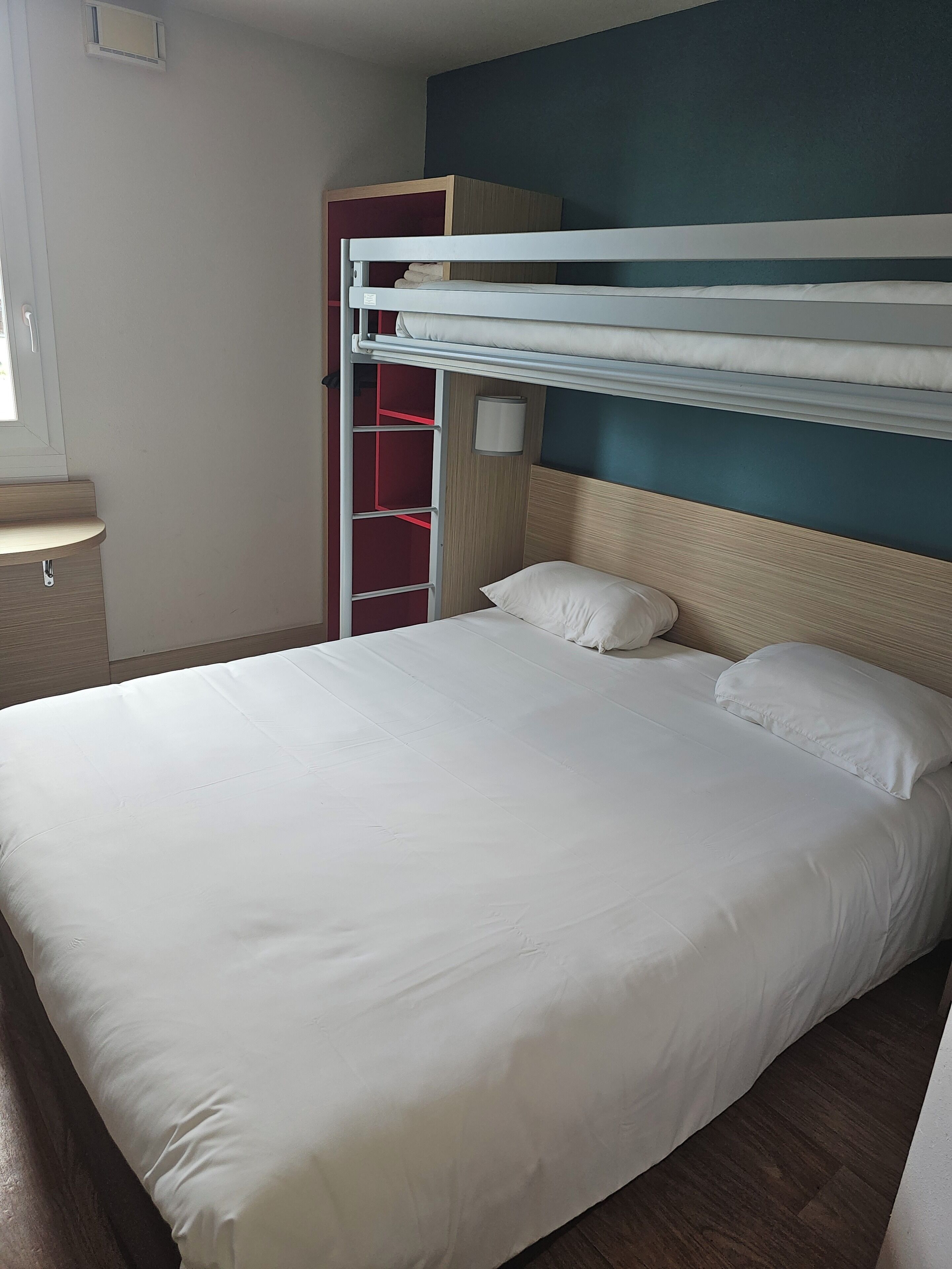 A bunk bed with white bedding, a wooden headboard, and a red wardrobe with shelves.