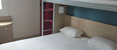 A bunk bed with white bedding, a wooden headboard, and a red wardrobe with shelves.