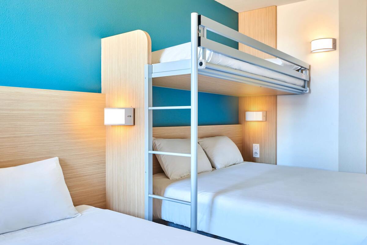 Een slaapkamer met een stapelbed, een houten hoofdbord, twee bedlampjes en een lichtschakelaar aan de muur.