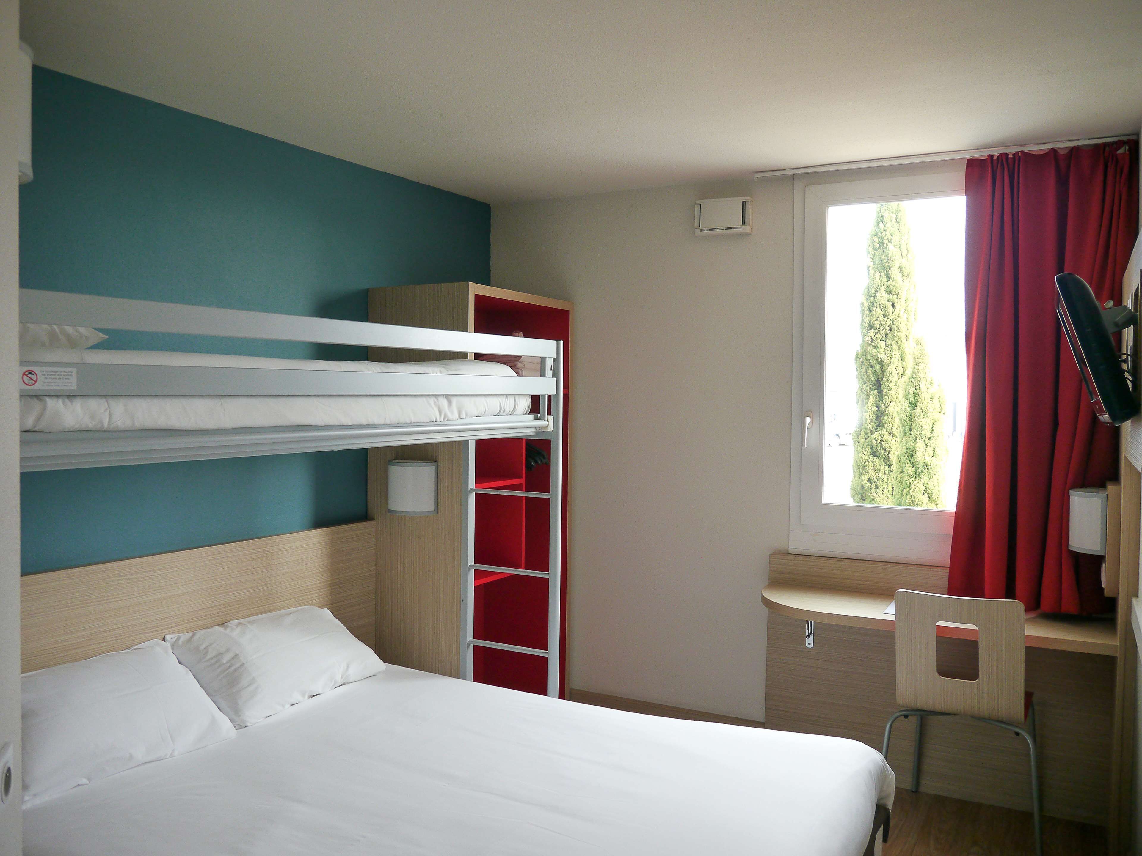Una habitación con una cama individual doble, un escritorio con silla, un armario rojo y una ventana con cortinas.