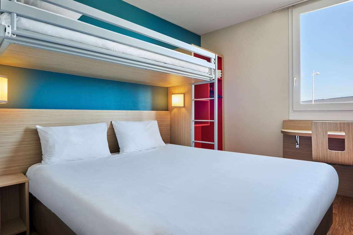 Een hotelkamer met een stapelbed, een houten hoofdbord, een nachtkastje, een rode opbergkast en een raam met uitzicht.