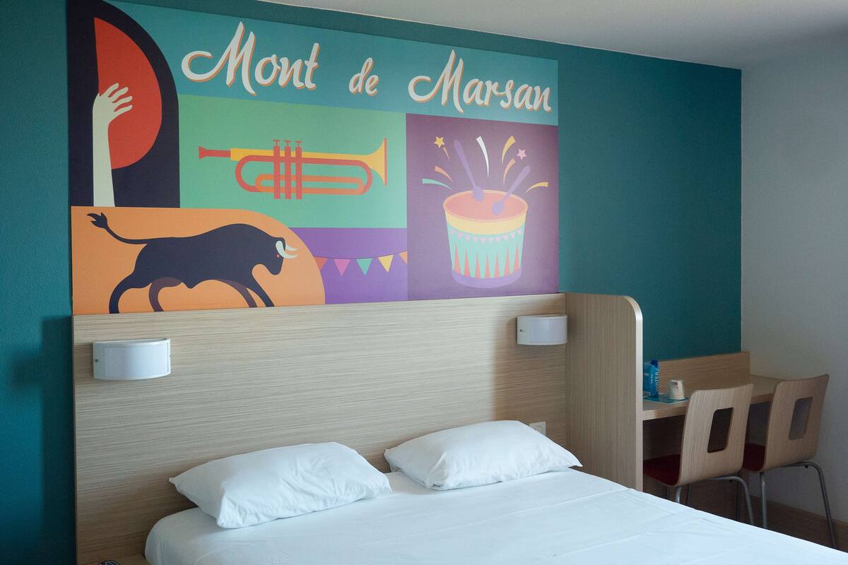 Hotelkamer met een bed, hoofdeinde, muur met kleurrijke muurschildering, bureau en twee stoelen.