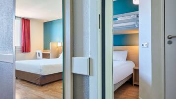 A hotel room with a bed, a bedside table, a lamp, and a window with a red curtain.